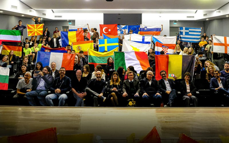 Auditório cheio de participantes com as bandeiras dos seus países
