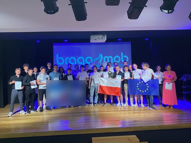 Grupo com as bandeiras da Polónia e da União Europeia no palco, com os certificados